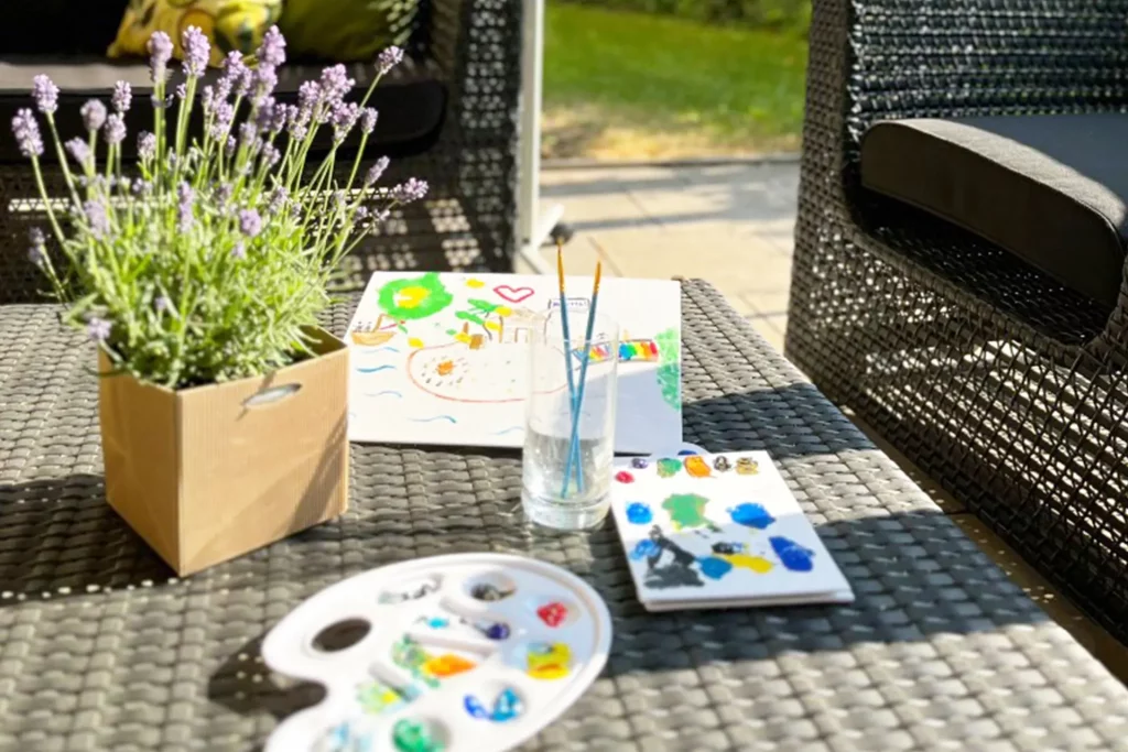 Tisch mit Wasserglas, Pinseln, Farbpalette und einer Zeichnung
