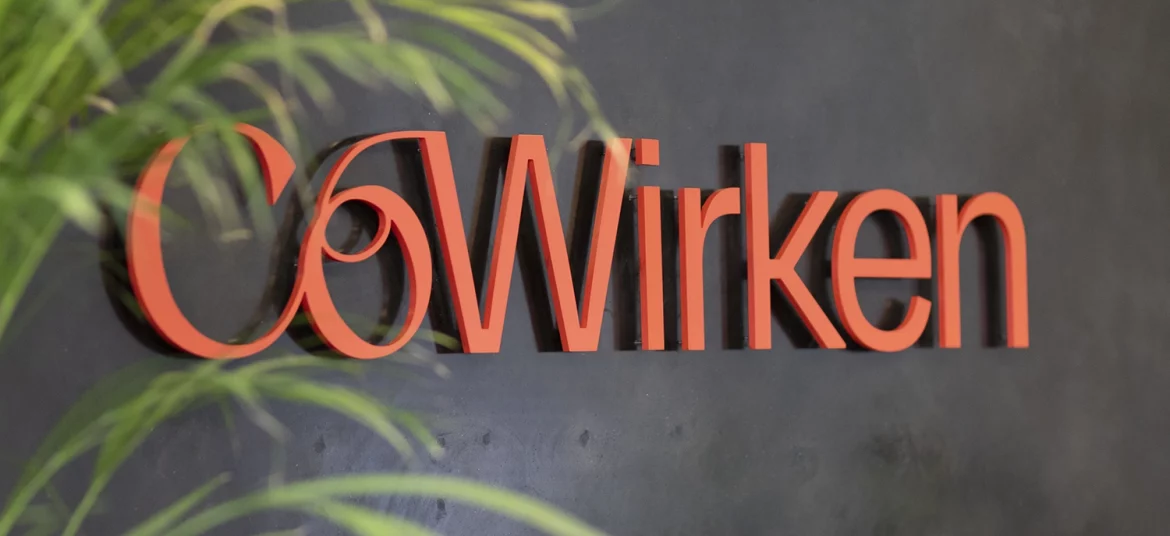 CoWirken-Logo in roter Schrift auf dunkler Wand, umgeben von grünen Pflanzen