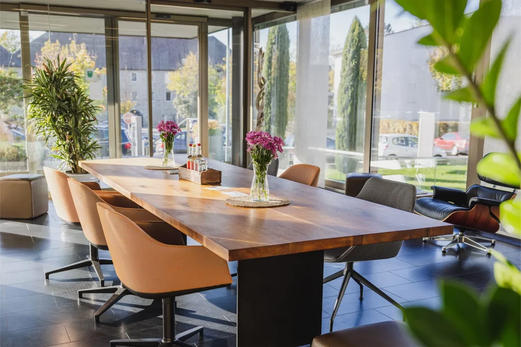 Helle Lobby im Erdgeschoss des Coworking Spaces mit großem Nussbaumtisch, modernen Stühlen und bodentiefen Fenstern