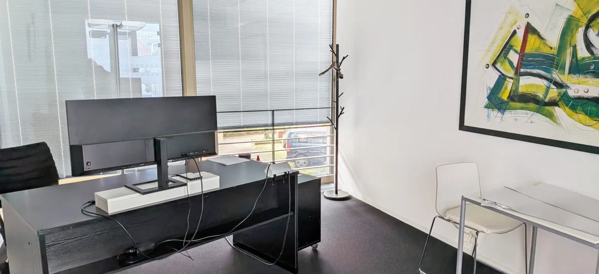 Helles, stilvoll eingerichtetes Büro mit schwarzen Schreibtisch, Monitor und abstraktem Wandbild. Es handelt sich hierbei um eine beispielhafte individuelle Ausstattung.