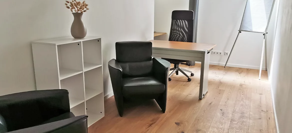 Komplett eingerichtetes Büro im Fokus-Bereich von CoWirken Schorndorf mit Schreibtisch, Flipchart, zwei bequemen Ledersesseln und Echtholzparkett.