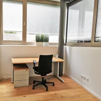 Heller Einzelarbeitsplatz im Private Office von CoWirken Schorndorf mit Schreibtisch aus Holz, ergonomischem Bürostuhl, Rollcontainer und großen Fenstern mit Jalousien.