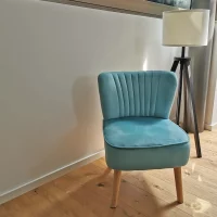 Gemütliche Sitzecke bei CoWirken Schorndorf mit einem hellblauen Samtsessel, einer dreibeinigen Stehlampe und Blick auf den Zugang zur Gartenlounge.